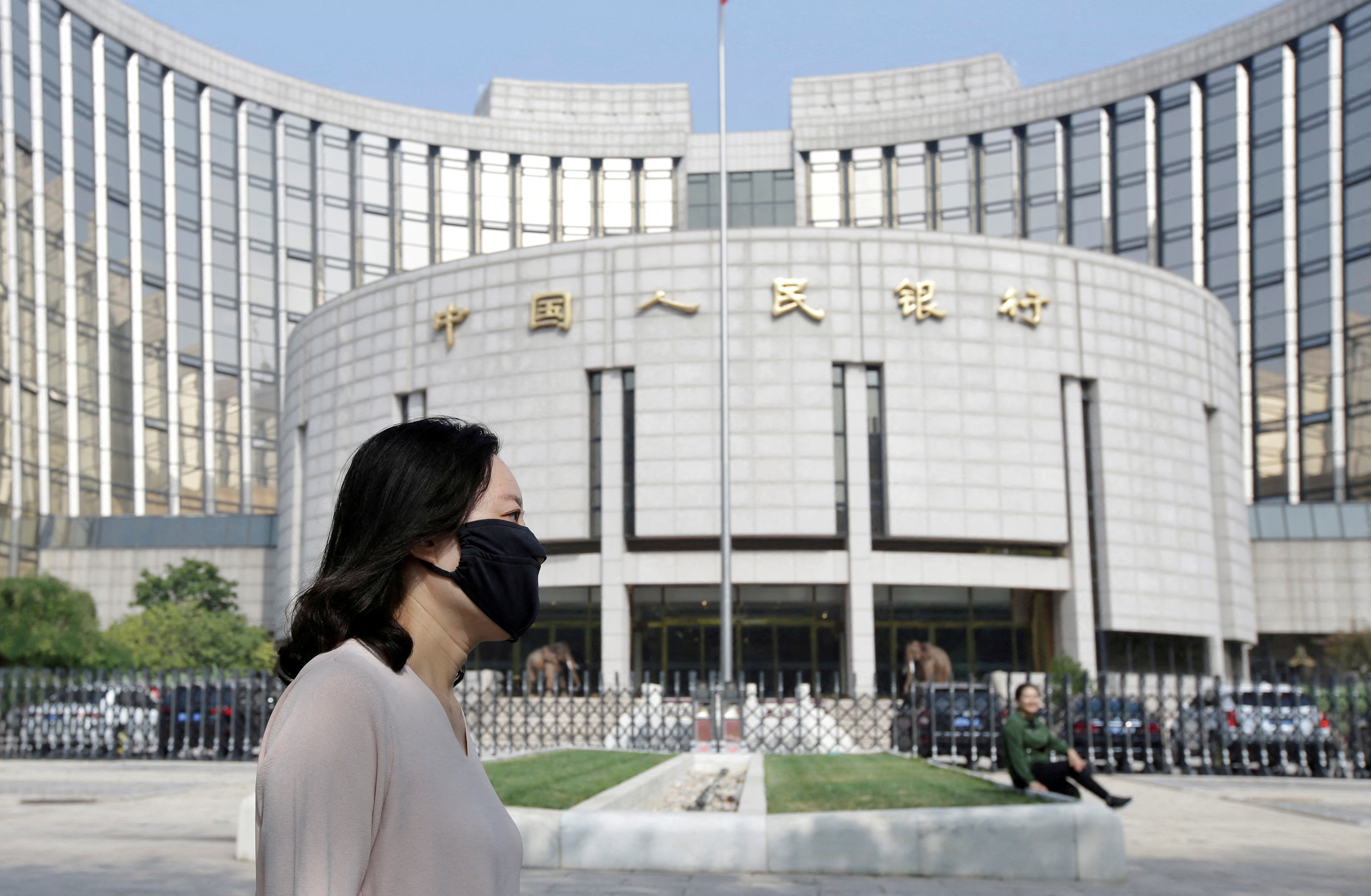 A woman walks past the headquarters of the PBOC, the central bank, in Beijing